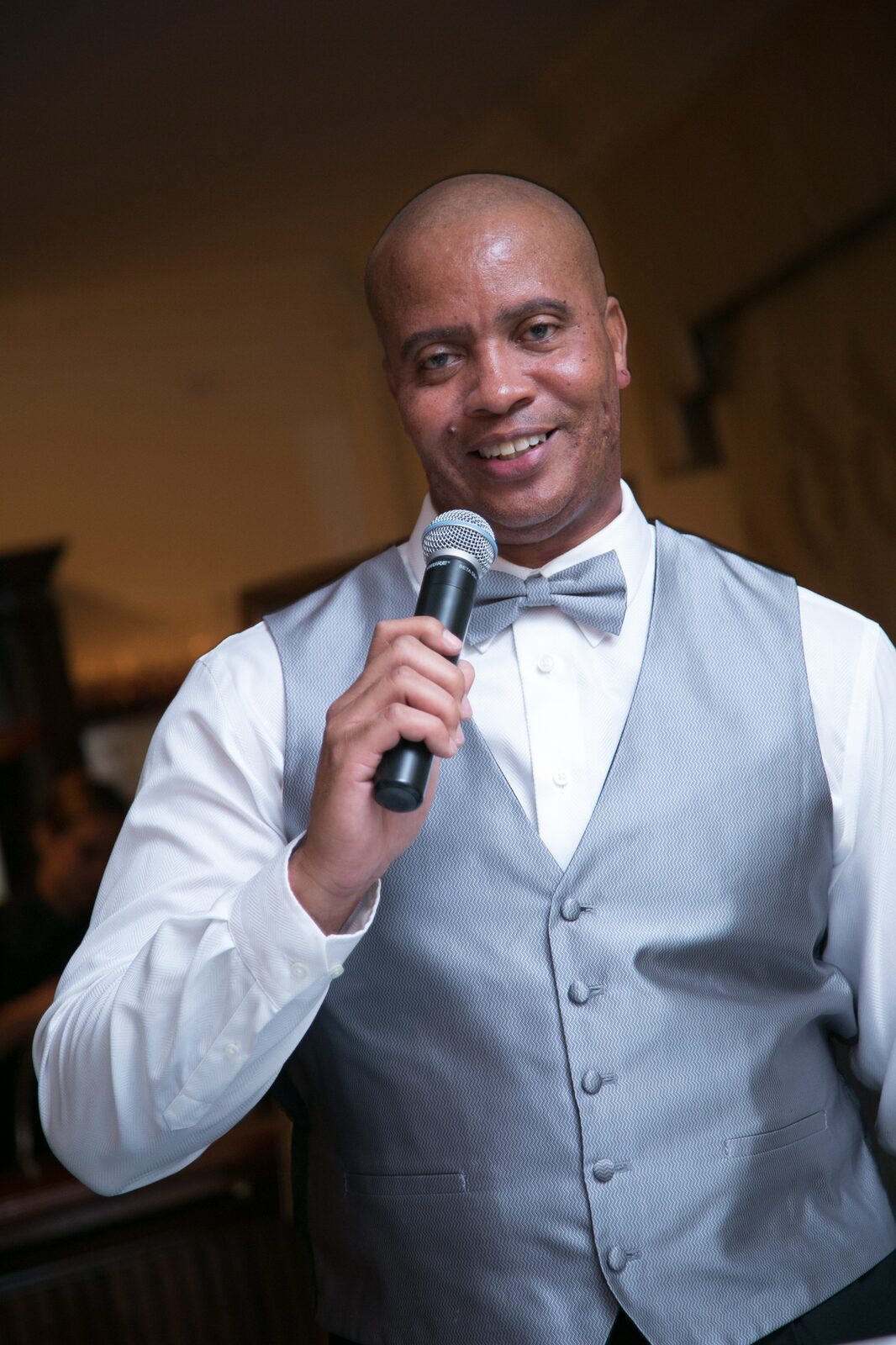 Ty Wilson in a silver vest and bow tie holding a microphone