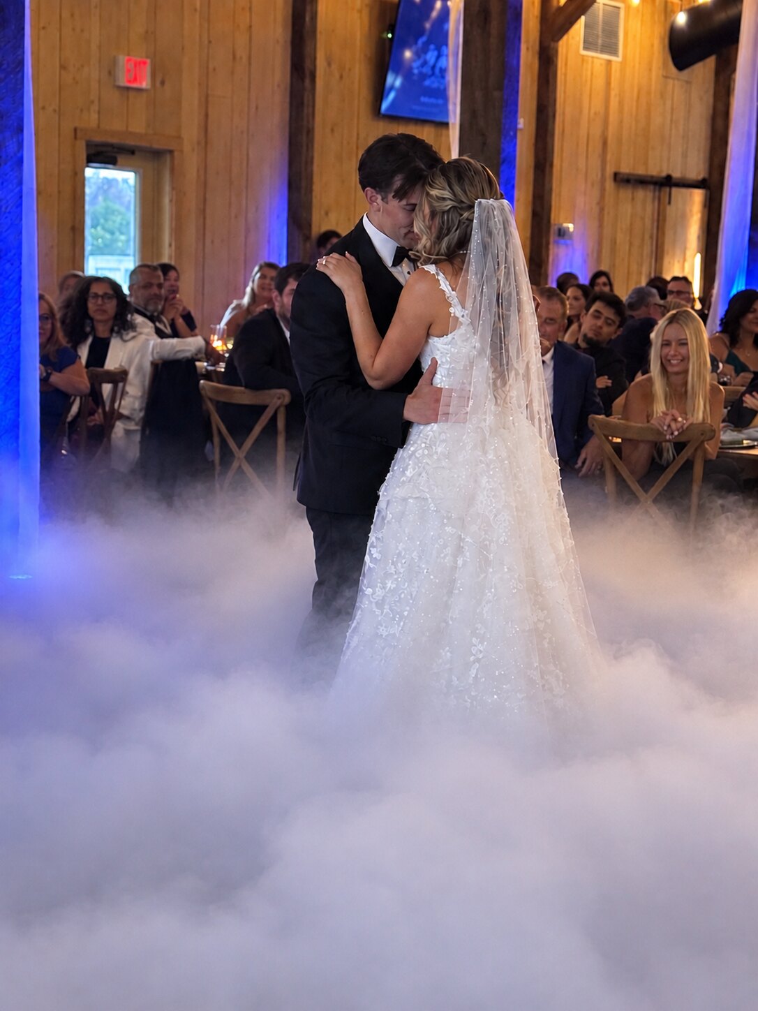 Bride and groom sharing a first dance on a floor of low fog under blue uplighting